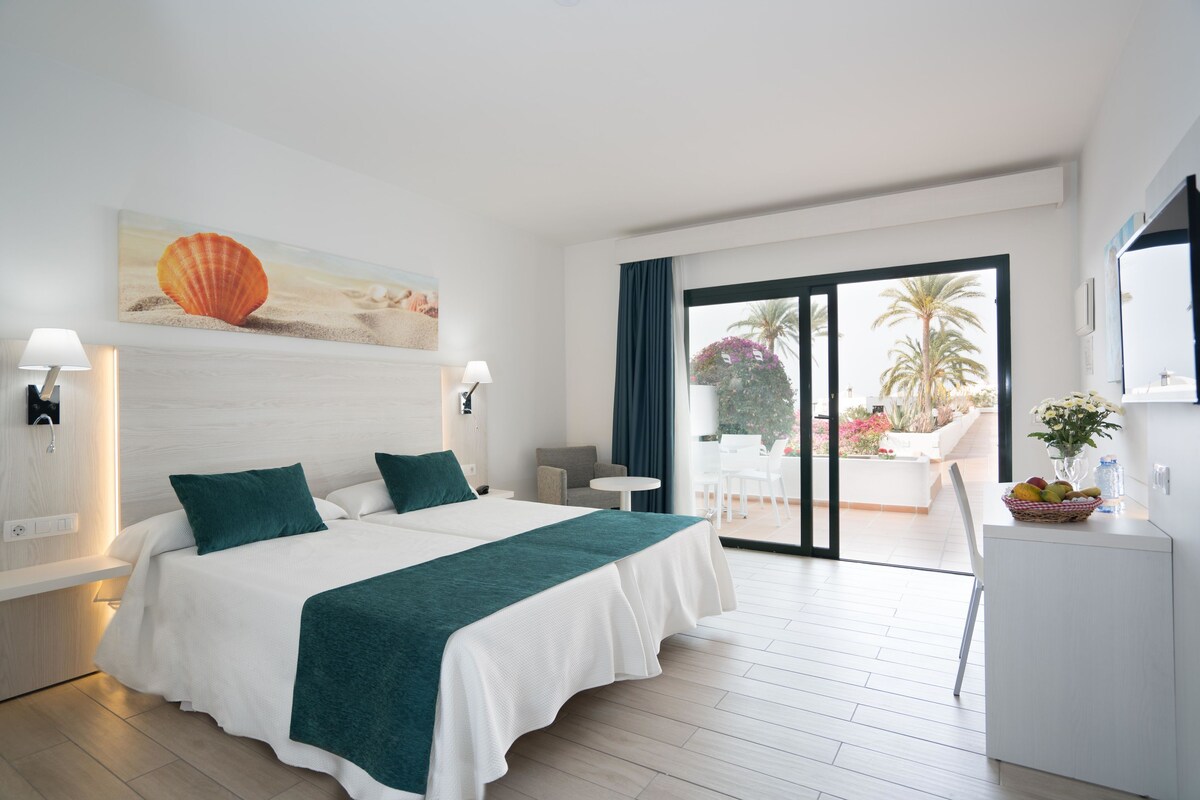 A hotel room with a large bed, a view of the outdoors, a desk, and a chair.