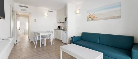 Una sala de estar moderna con un sofá color turquesa, una mesa de centro blanca y una zona de comedor con una mesa y sillas blancas.