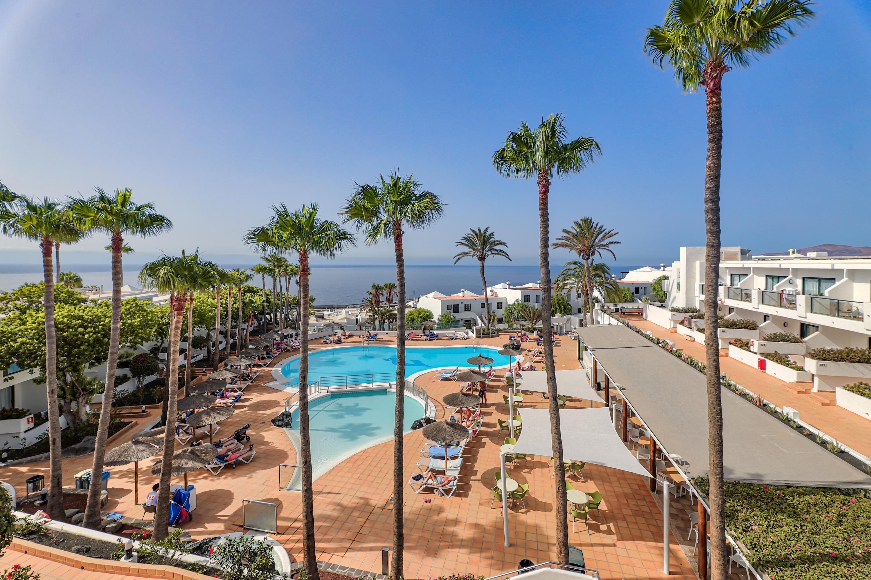 A resort with a large pool, palm trees, and a view of the sea.