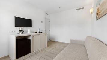 A modern living room with a flat-screen TV, a coffee maker, and a small refrigerator.
