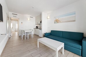 A modern living room with a teal sofa, a white coffee table, and a dining area with a white table and chairs.