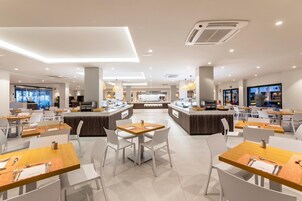 Un comedor moderno con varias mesas y sillas, una barra central y una cocina al fondo.