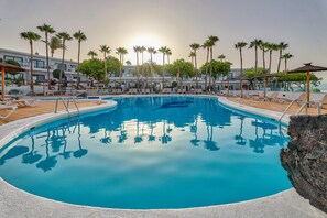 A swimming pool with lounge chairs and palm trees, surrounded by a building with balconies.