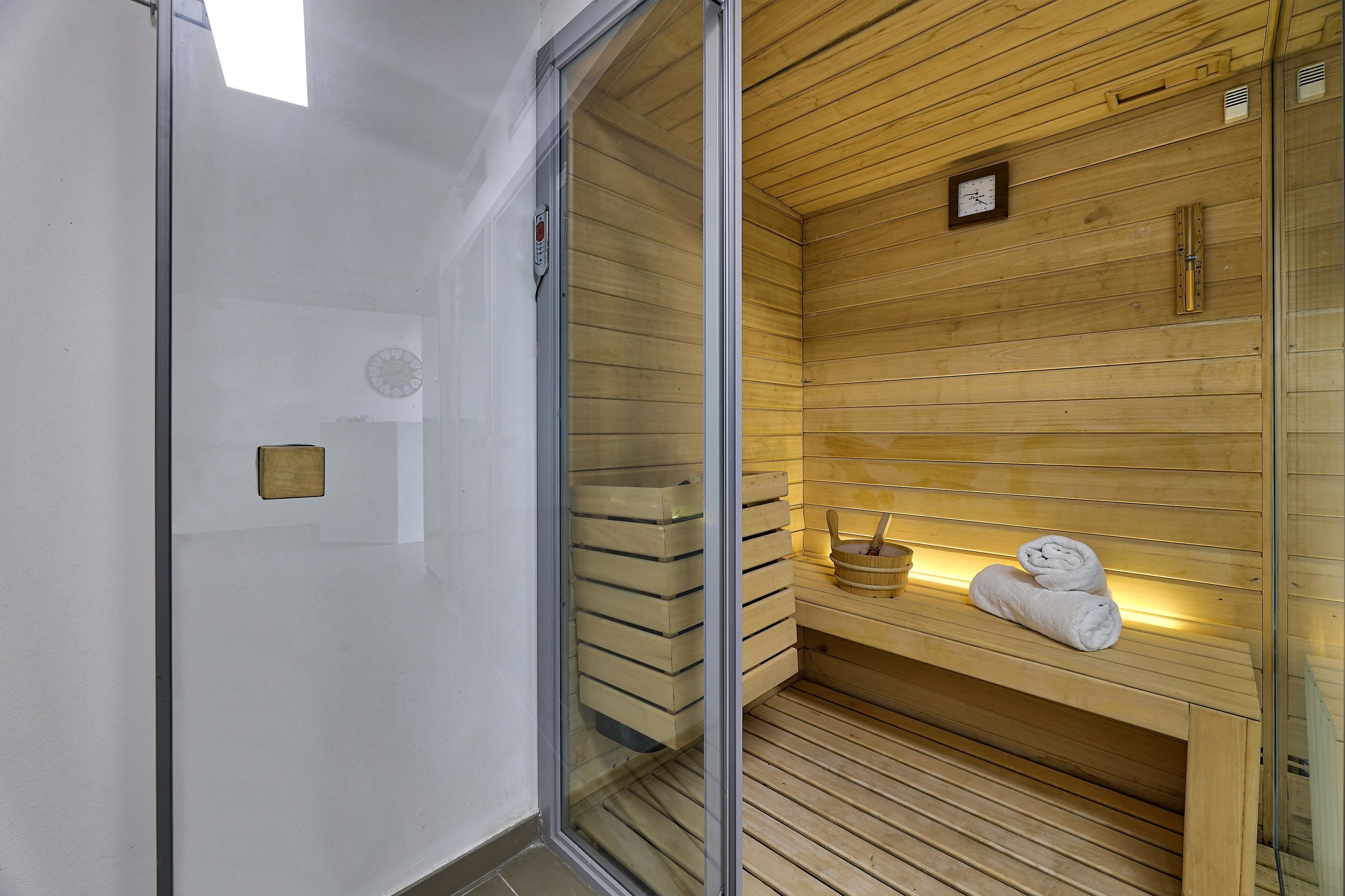 A sauna with wooden walls and a bench, a clock, and towels on the bench.