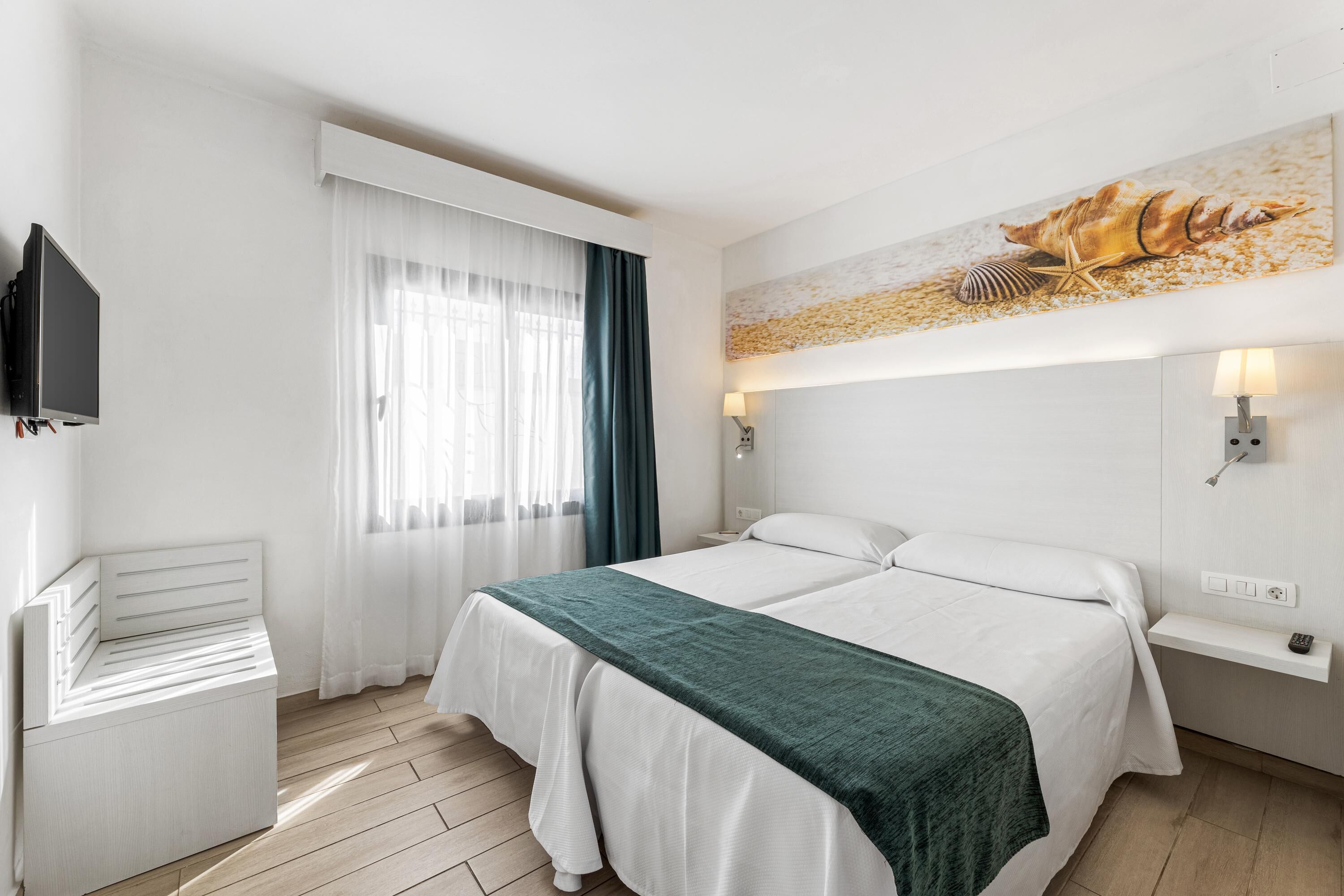 Ein Hotelzimmer mit Bett, Fernseher, Schreibtisch und einem Fenster mit Vorhängen.