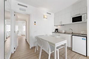 A modern kitchen with white cabinetry, a built-in microwave, and a coffee maker. There is a dining table with chairs in the center of the room.