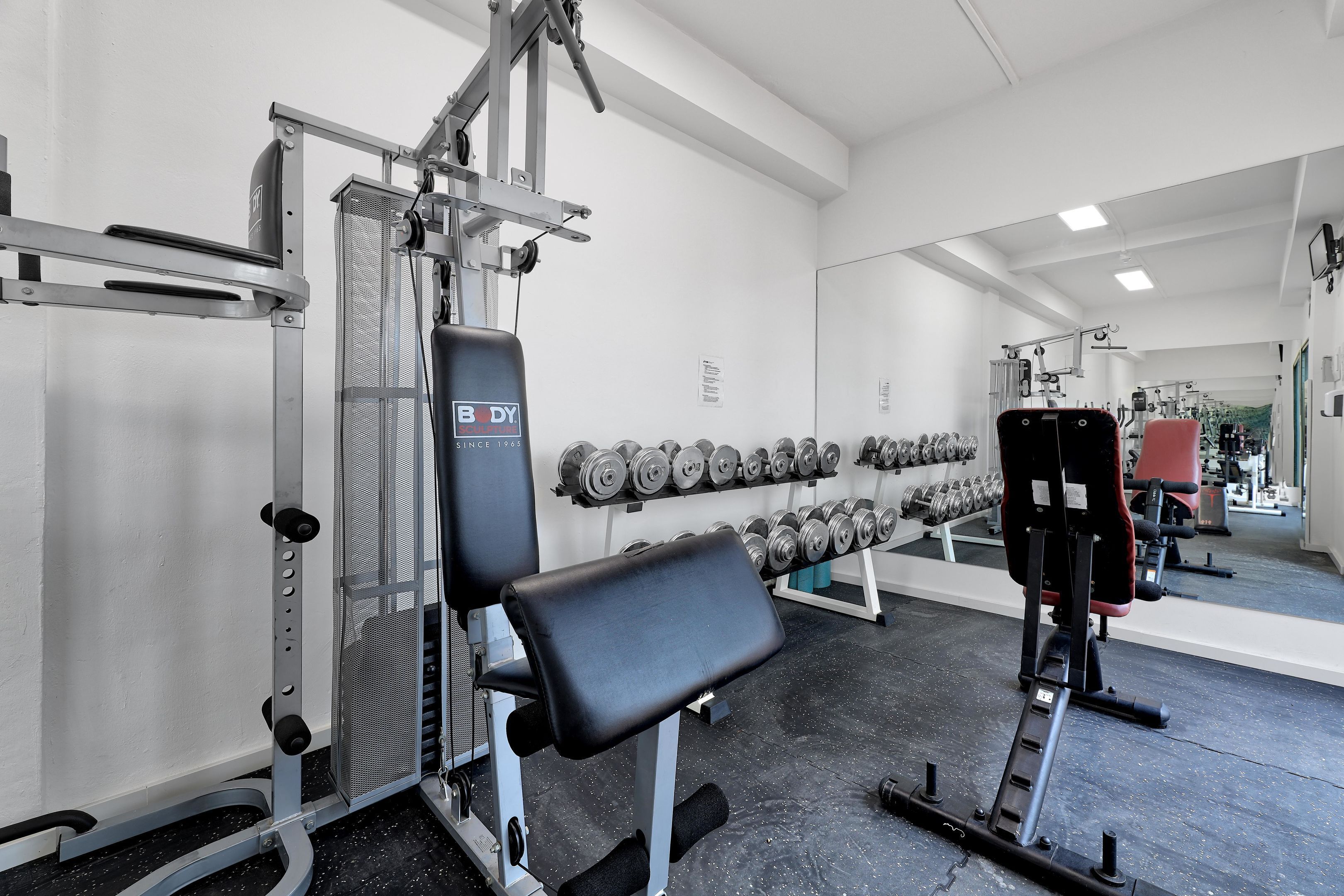 Un gimnasio con equipo de levantamiento de pesas, mancuernas y un banco.