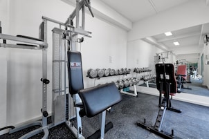 Un gimnasio con equipo de levantamiento de pesas, mancuernas y un banco.