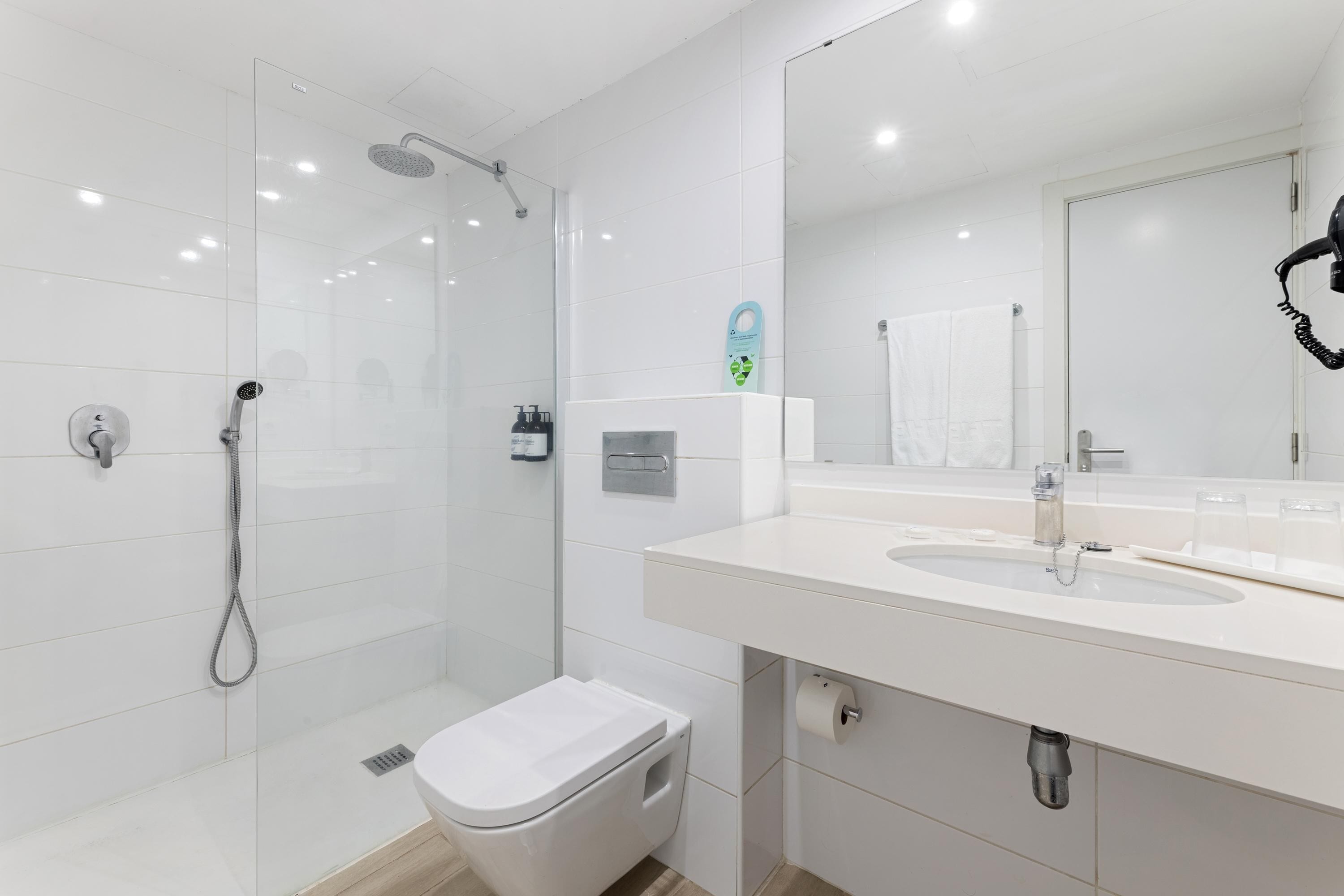 Un baño moderno con ducha de vidrio, un lavabo blanco con espejo y un inodoro.