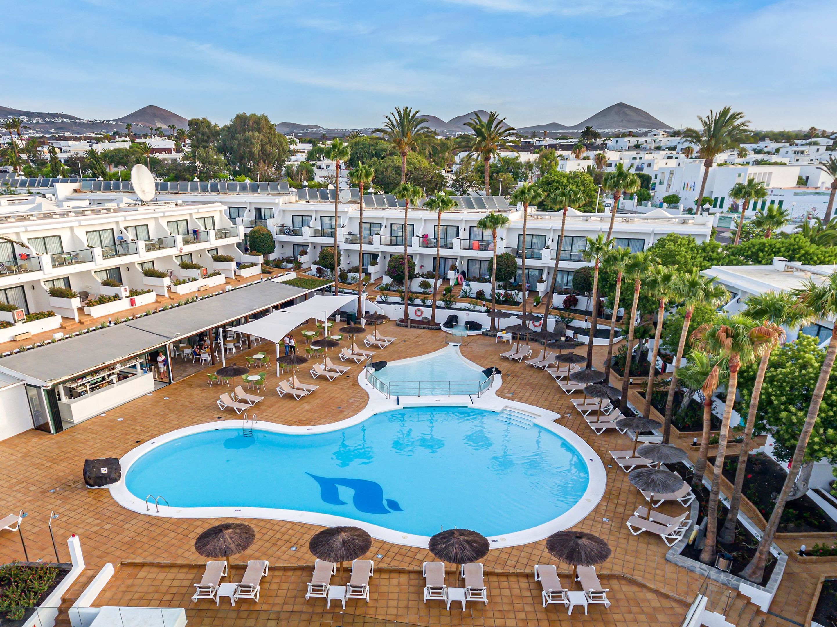 A resort with a large pool, sun loungers, and palm trees.