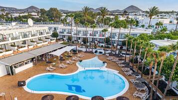 A resort with a large pool, sun loungers, and palm trees.