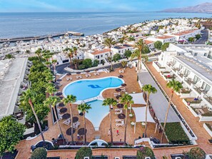 A resort with a central swimming pool surrounded by sun loungers and umbrellas, white buildings, and a view of the sea. - THB Flora Aparthotel (Tías)