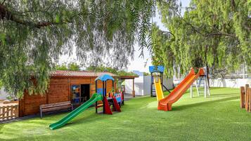 A playground with slides and a small wooden building, surrounded by trees.