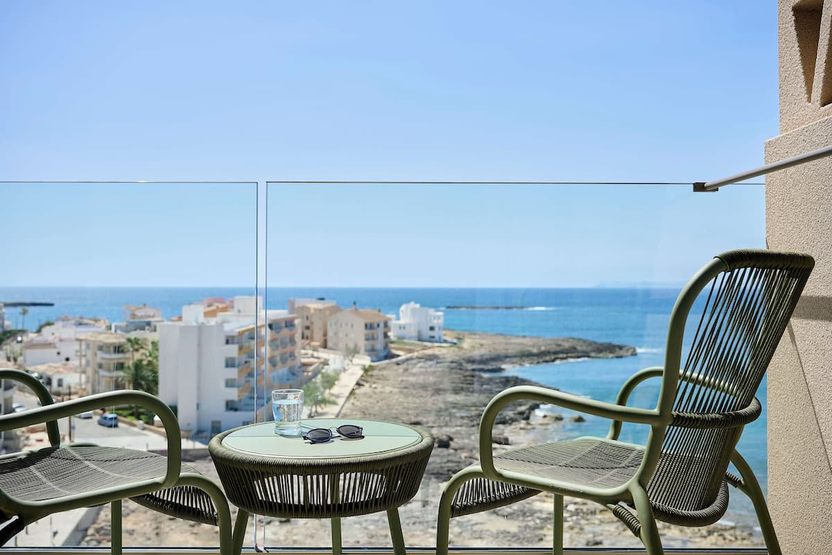Un balcon avec deux fauteuils en osier et une petite table, d’où l’on peut admirer un littoral rocheux et des bâtiments.