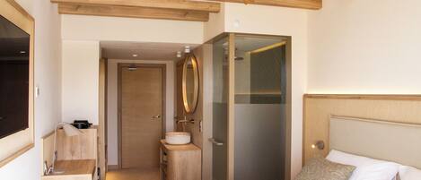 A modern hotel room with a wooden ceiling, a large bed, a bedside table, a mirror, and a glass shower enclosure.