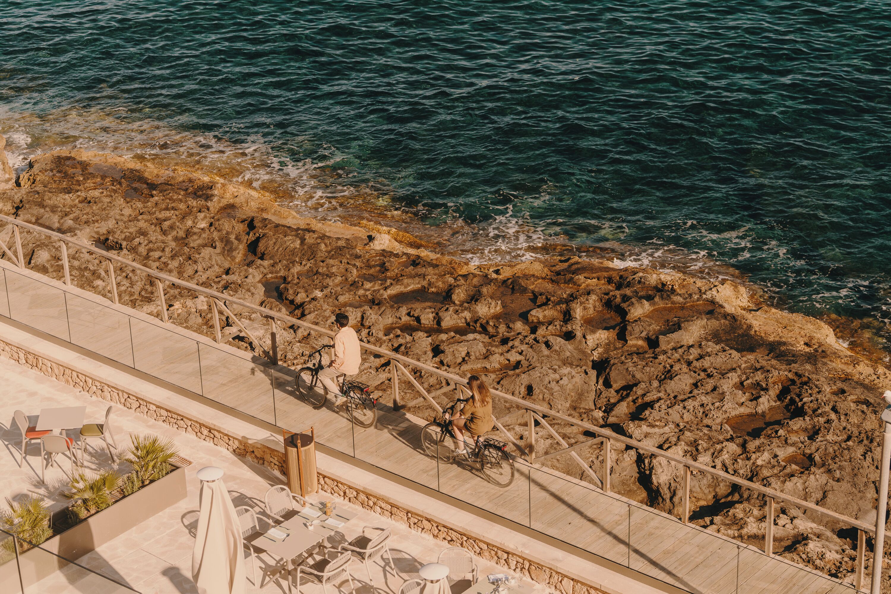 A rocky coastline with a paved walkway and outdoor seating area.
