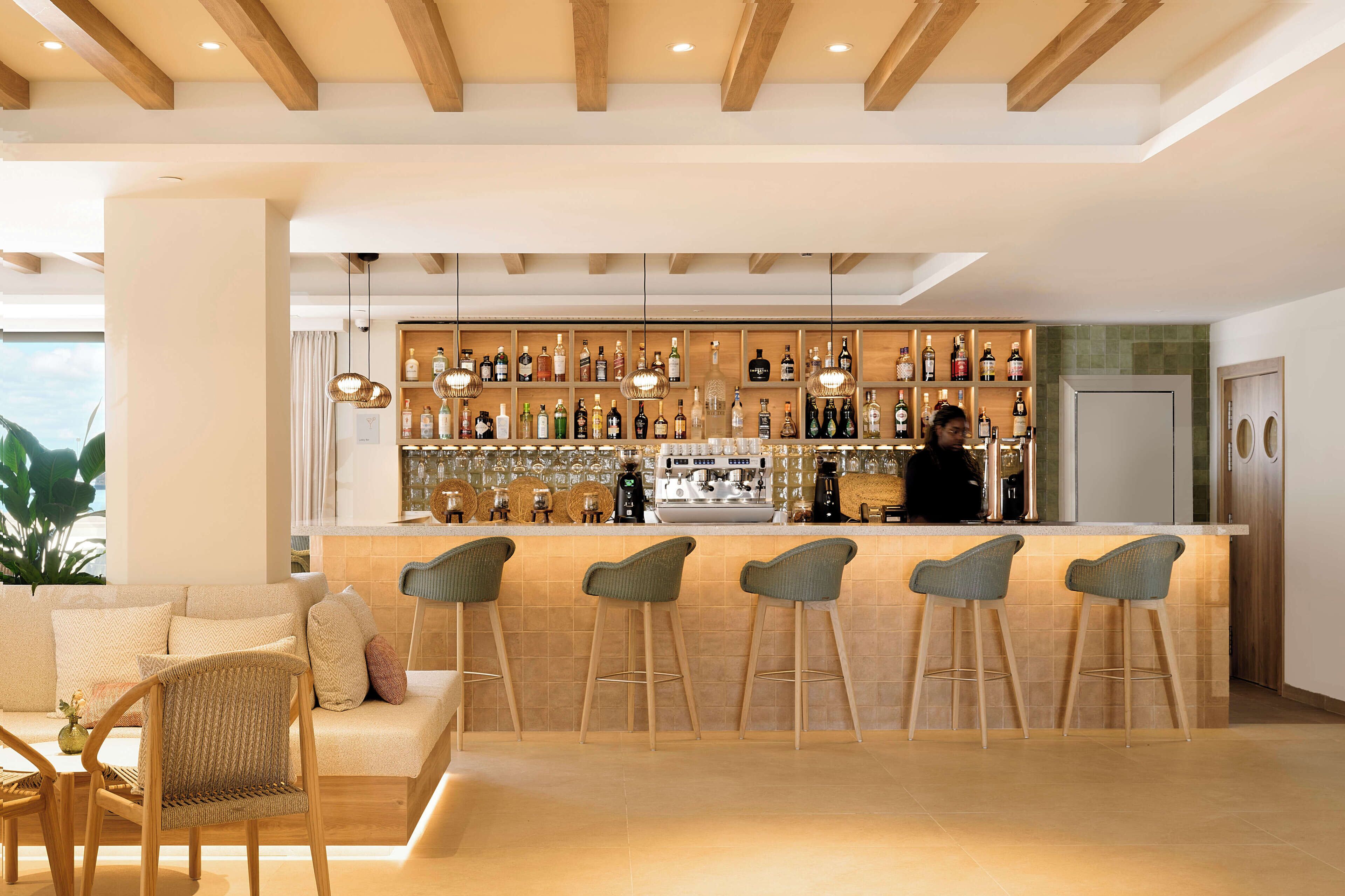 Zona de bar moderna con mostrador, taburetes y una variedad de botellas.