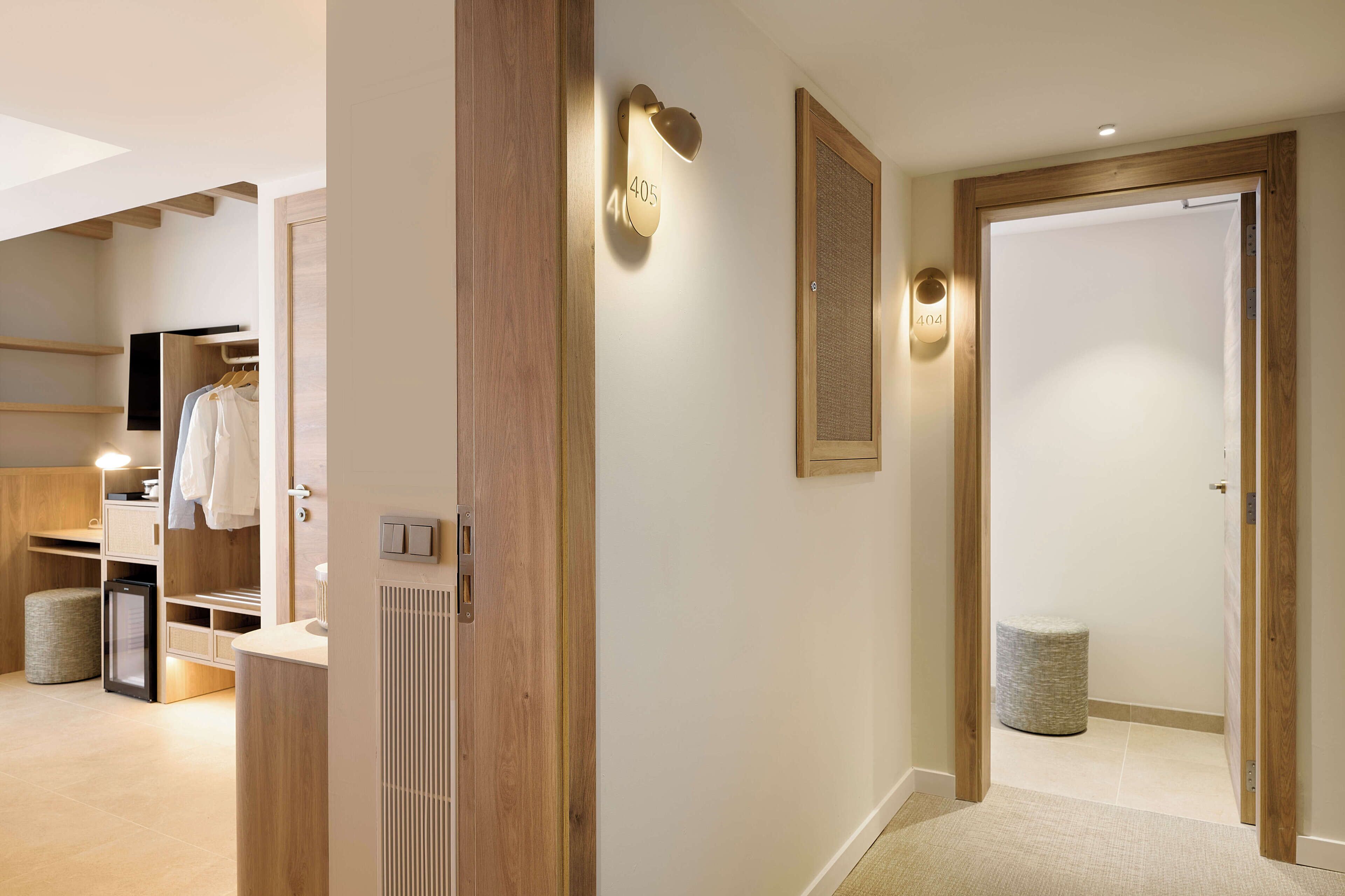 A modern hotel room with a wooden floor, a built-in wardrobe, a small kitchenette, and a cozy seating area.
