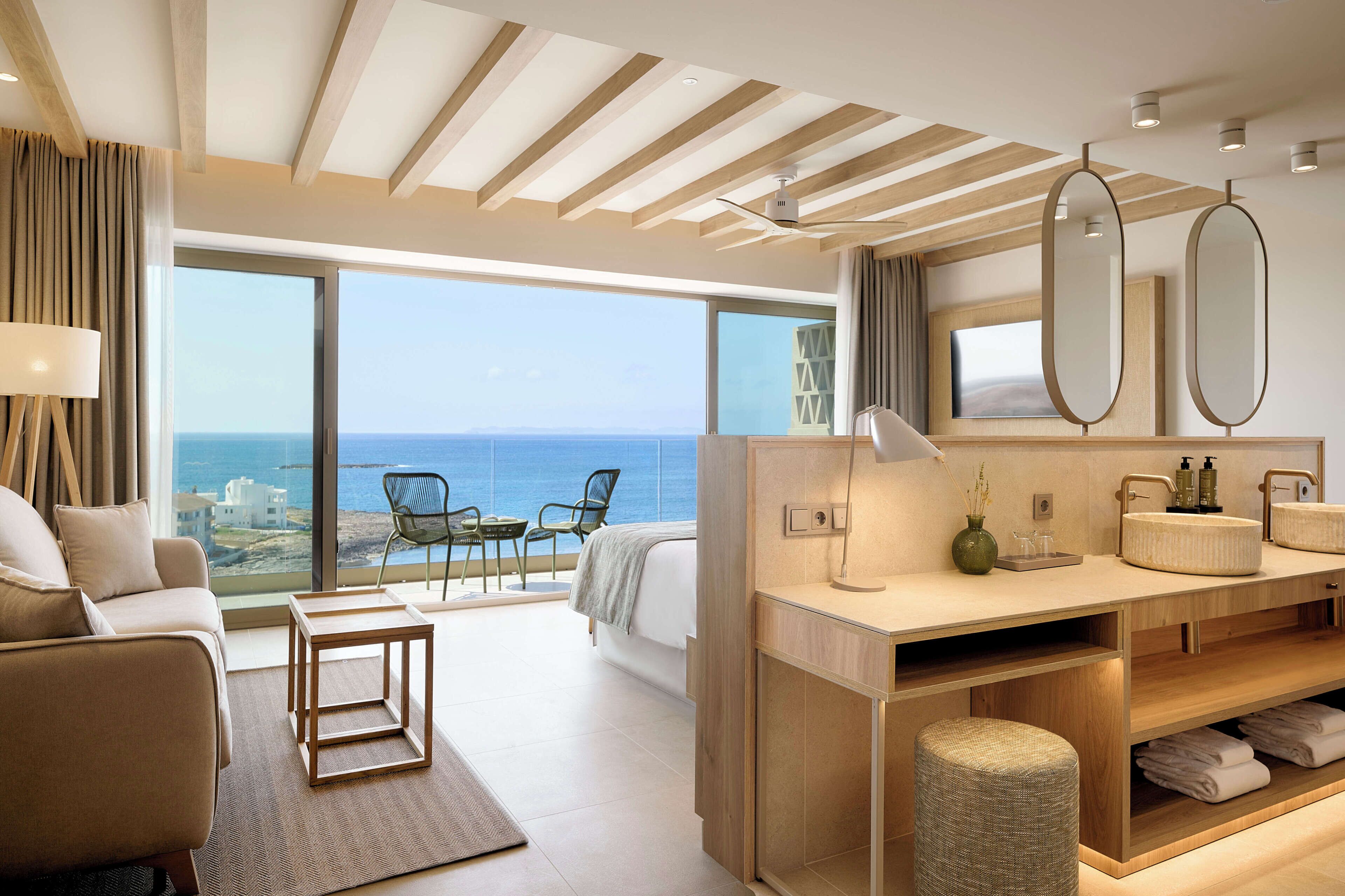A modern hotel room with a balcony, a sofa, a bed, a large mirror, and a wooden vanity.