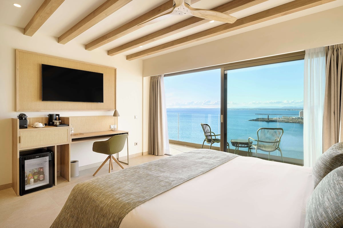 Une chambre d’hôtel avec un grand lit, un bureau avec une télévision, un mini-réfrigérateur et une vue sur la mer.