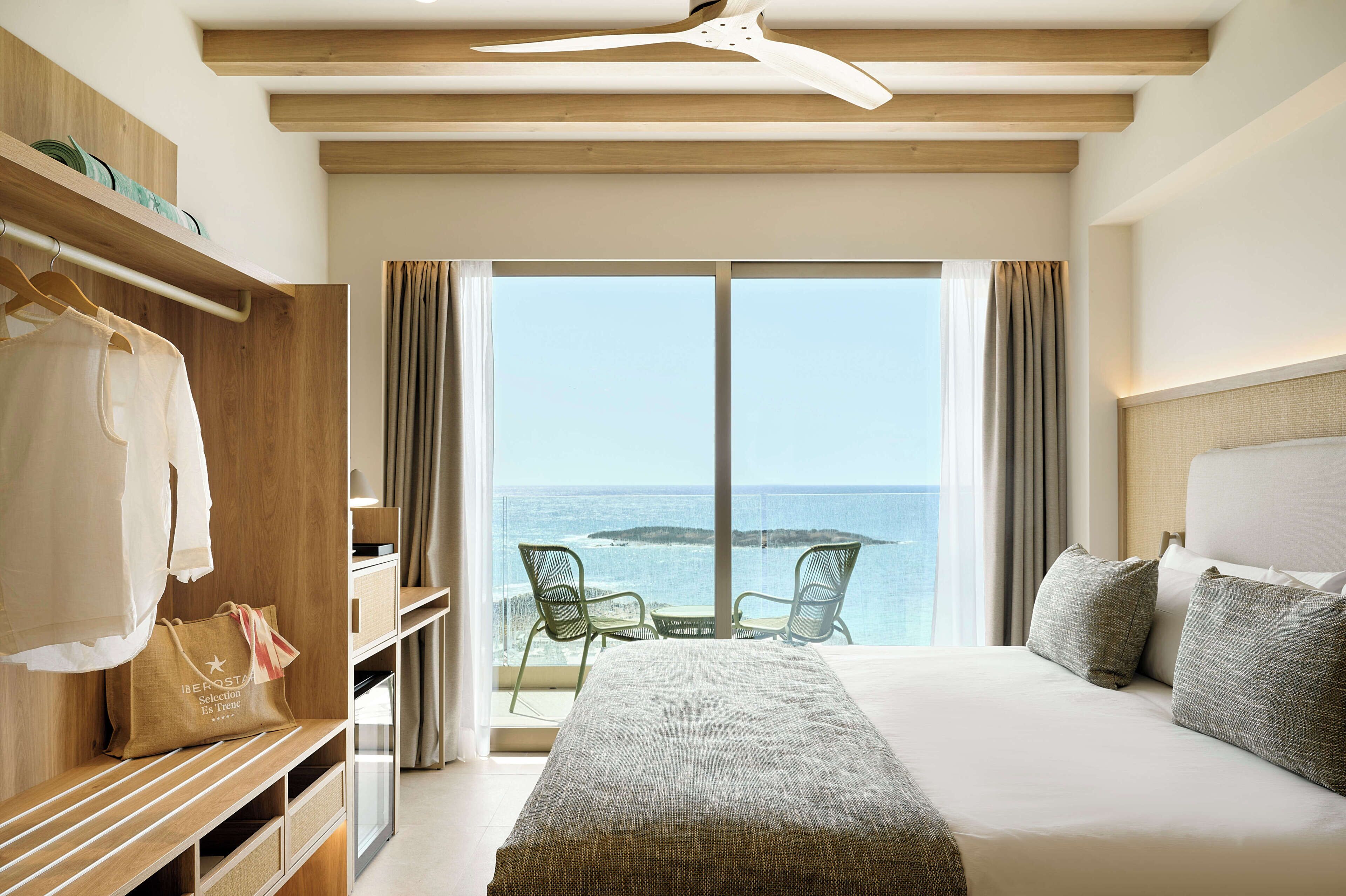 Habitación de hotel con cama, armario, zona de estar con vista al mar y balcón.