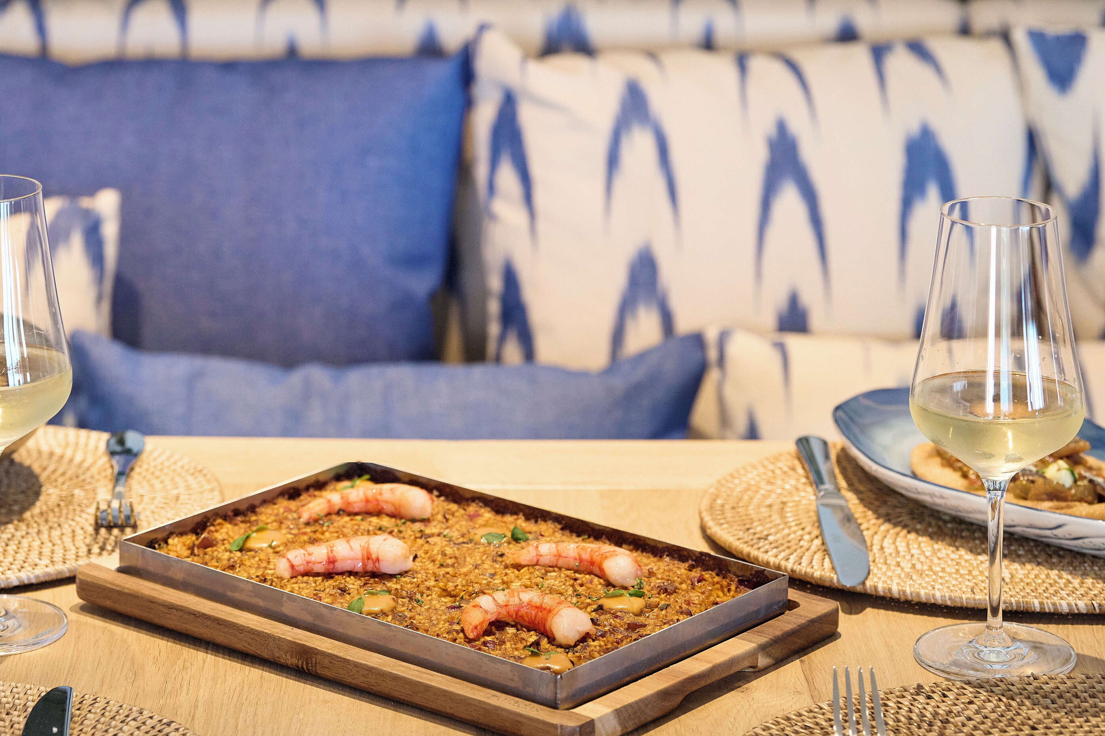 A dining table with a seafood dish, wine glasses, and a woven placemat.