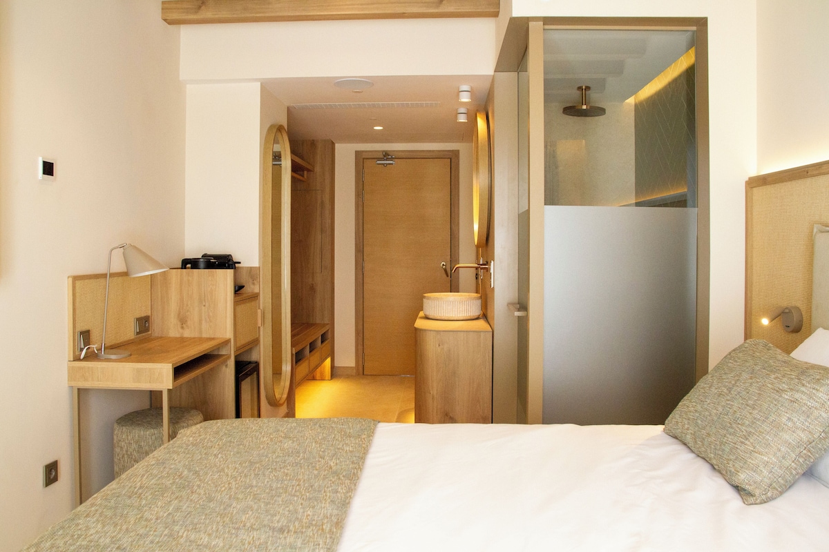 A modern hotel room with a bed, a desk, and a shower area.