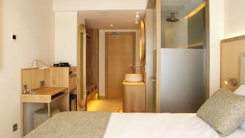 A modern hotel room with a bed, a desk, and a shower area.