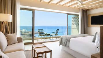 Quarto de hotel moderno com uma cama grande, um sofá, uma mesinha e uma varanda com vista para o mar.
