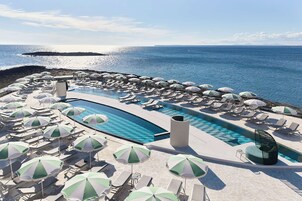 Zona junto a la piscina con tumbonas y sombrillas, con vistas al mar.