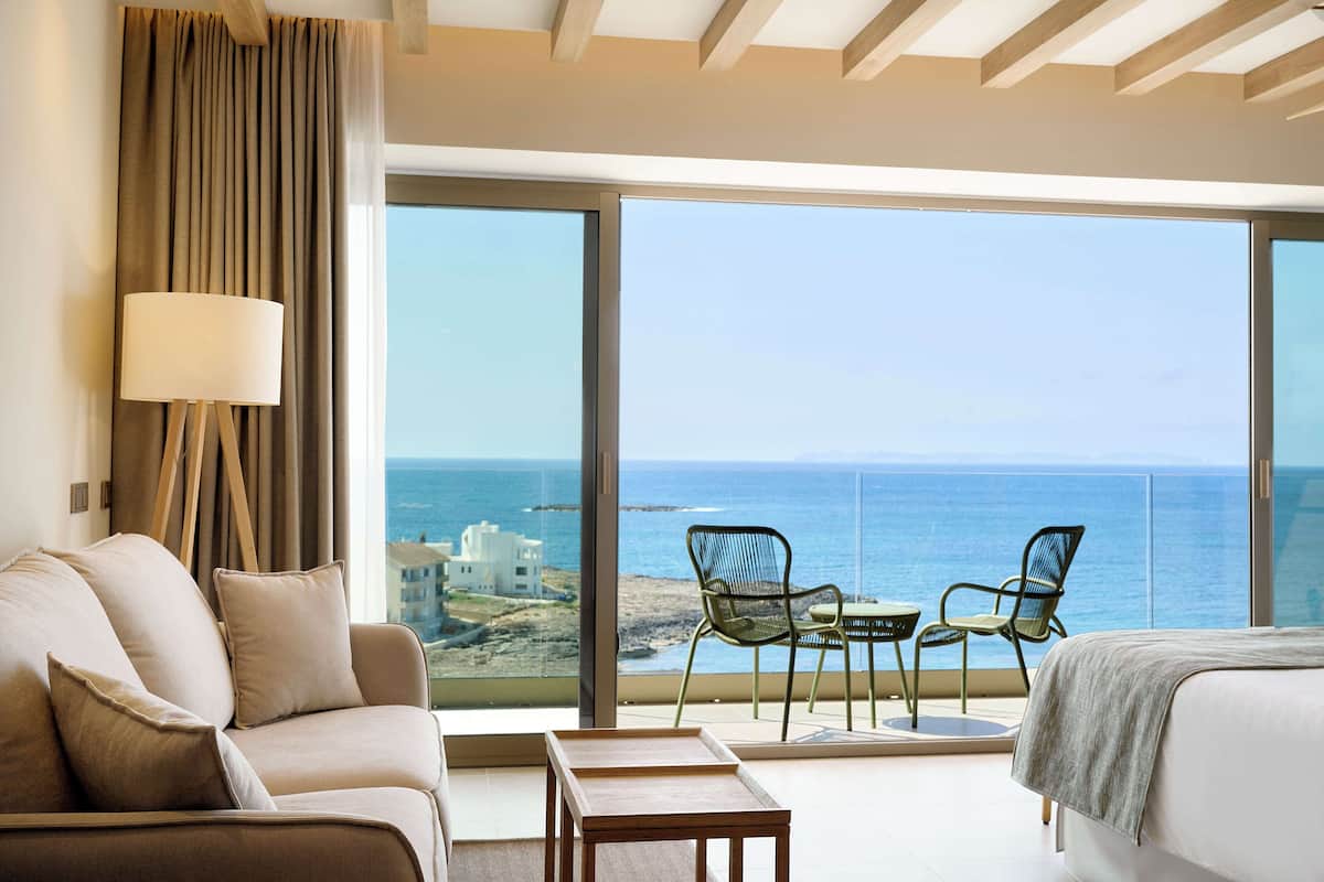 Une chambre d’hôtel avec une grande fenêtre, un canapé, un lit et une table avec des chaises.