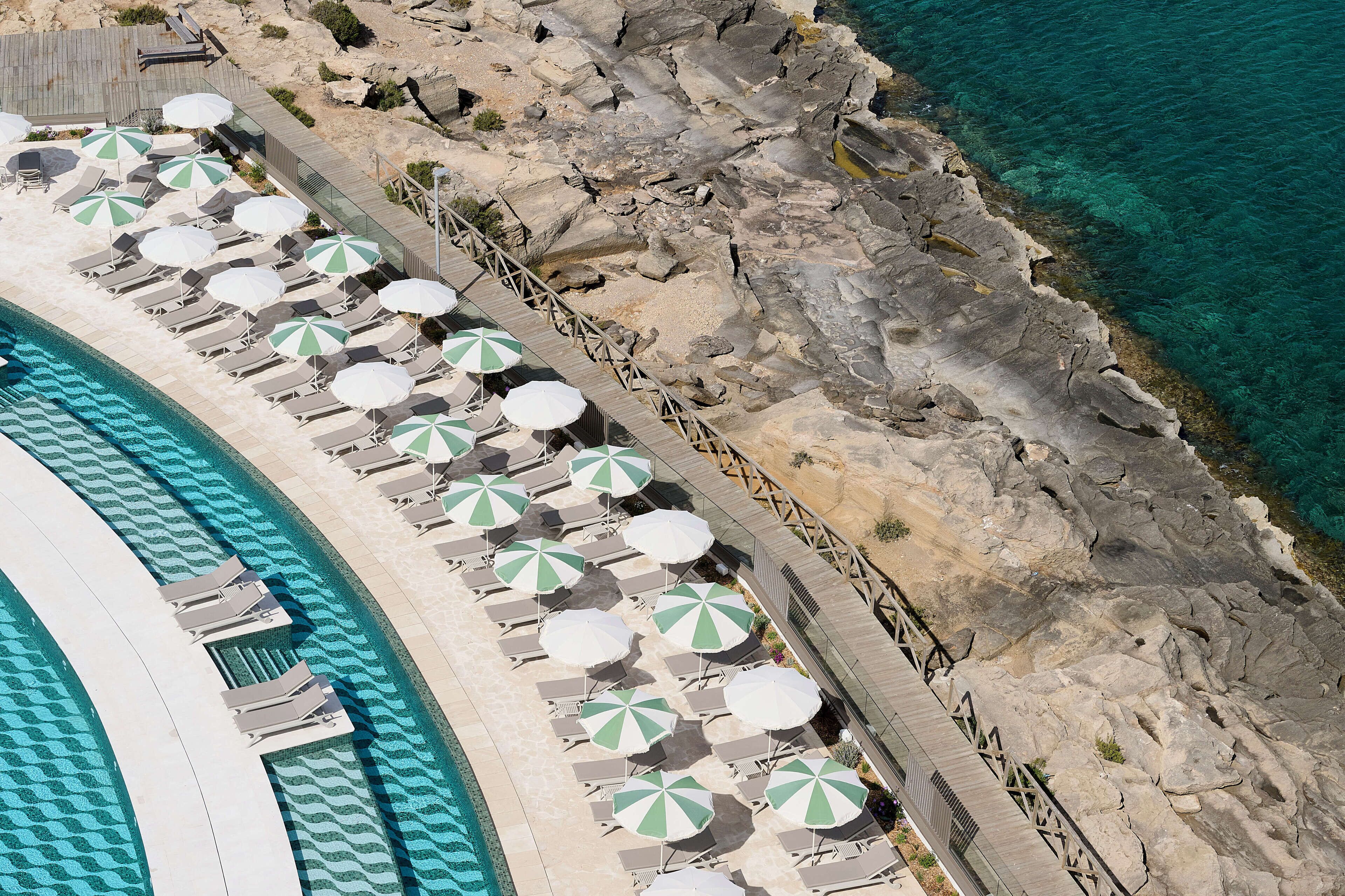 An aerial view of a resort with a pool, sun loungers, and umbrellas.