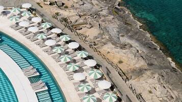 Eine Vogelperspektive zeigt ein Resort mit Pool, Liegestühlen und Sonnenschirmen.
