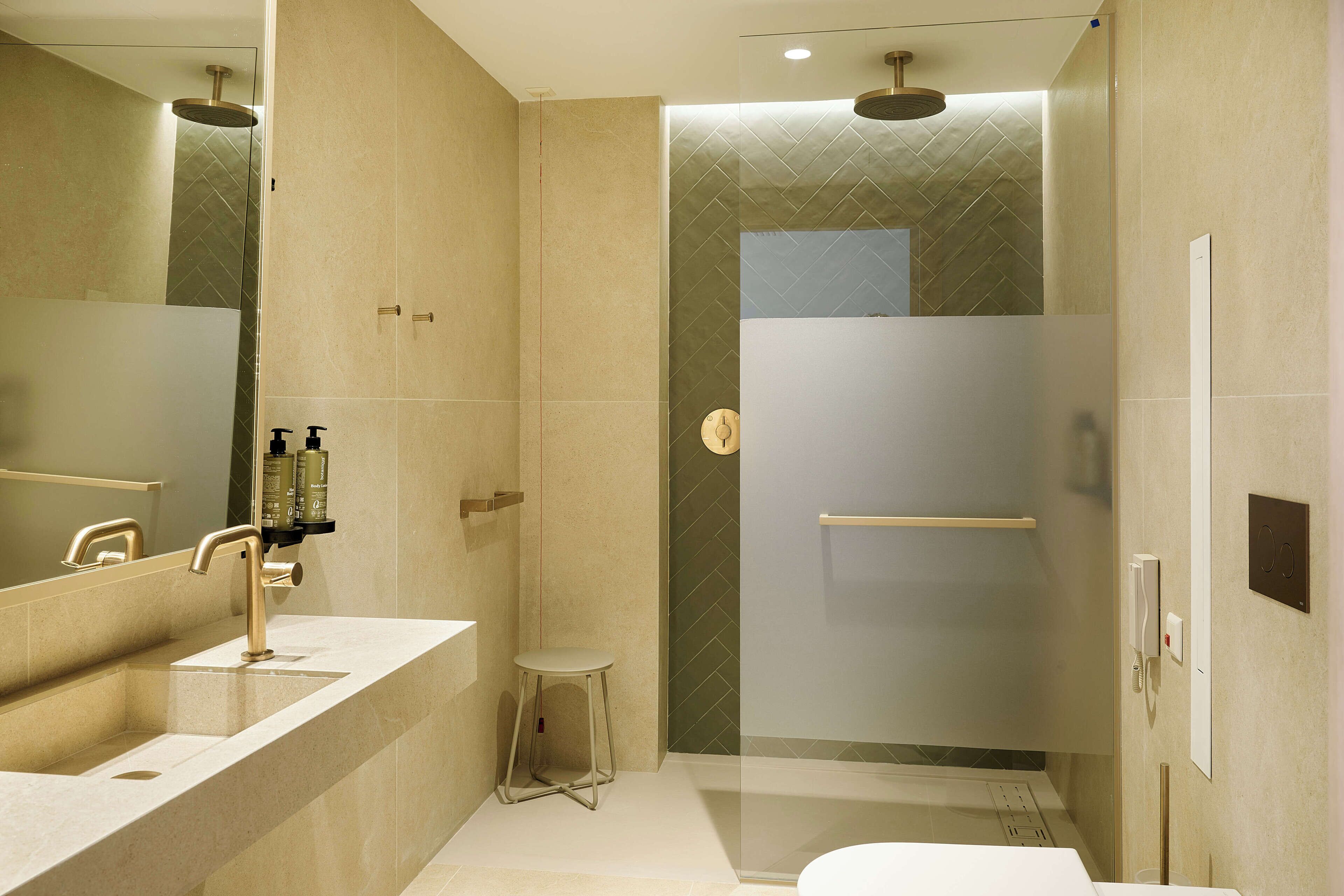 A modern bathroom with a large mirror, dual sinks, a glass-enclosed shower, and a small stool.