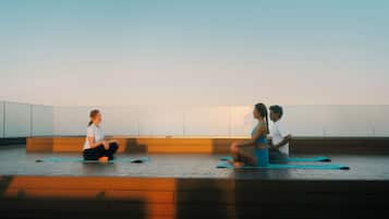 Tres personas sentadas sobre esterillas de yoga en una habitación amplia con suelo de madera y techo alto.