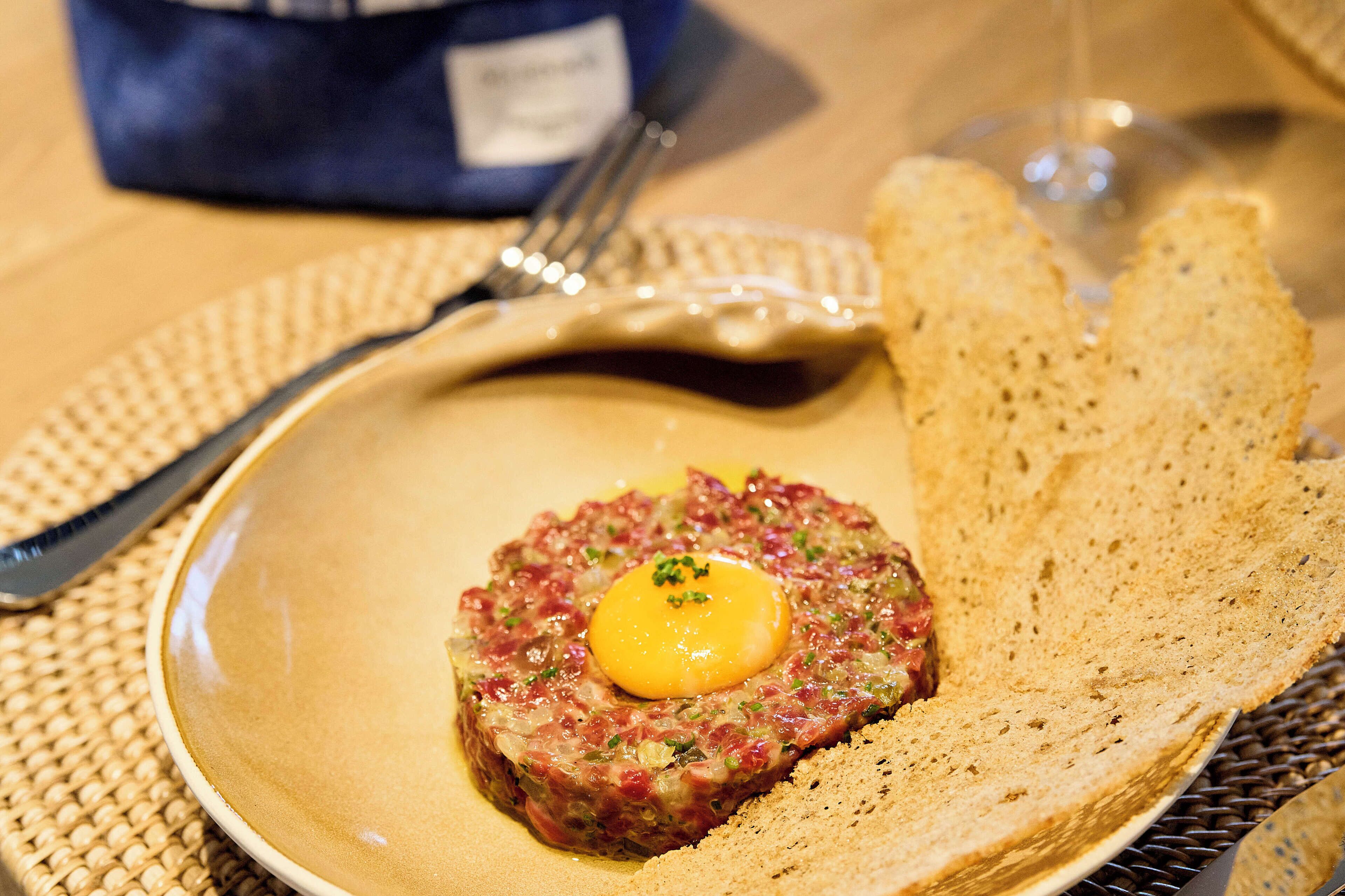 Un plato de tártara de carne con una yema de huevo crudo encima, acompañado de una rebanada de pan.