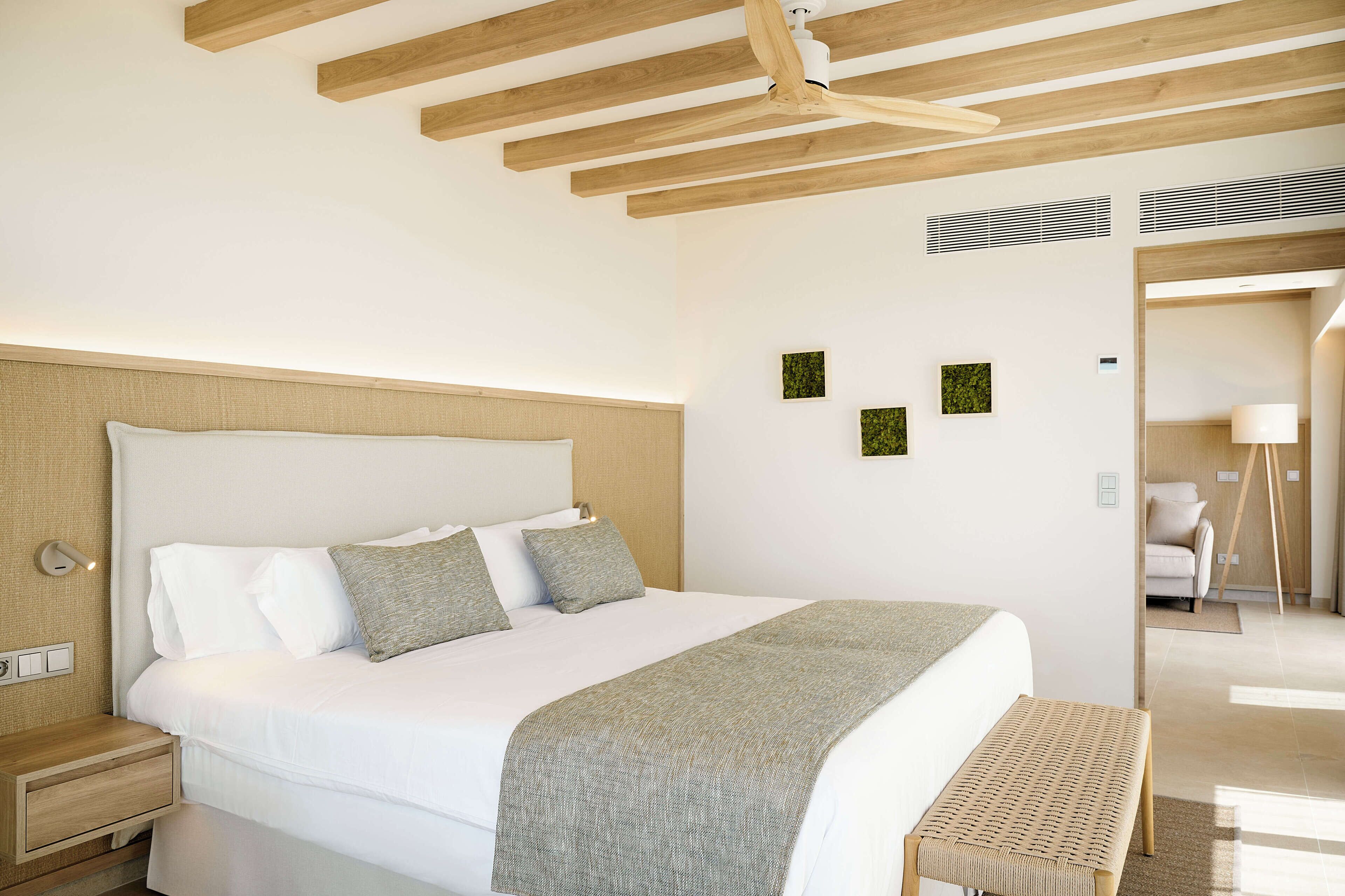 A modern bedroom with a large bed, wooden ceiling beams, a bedside table, and a bench.