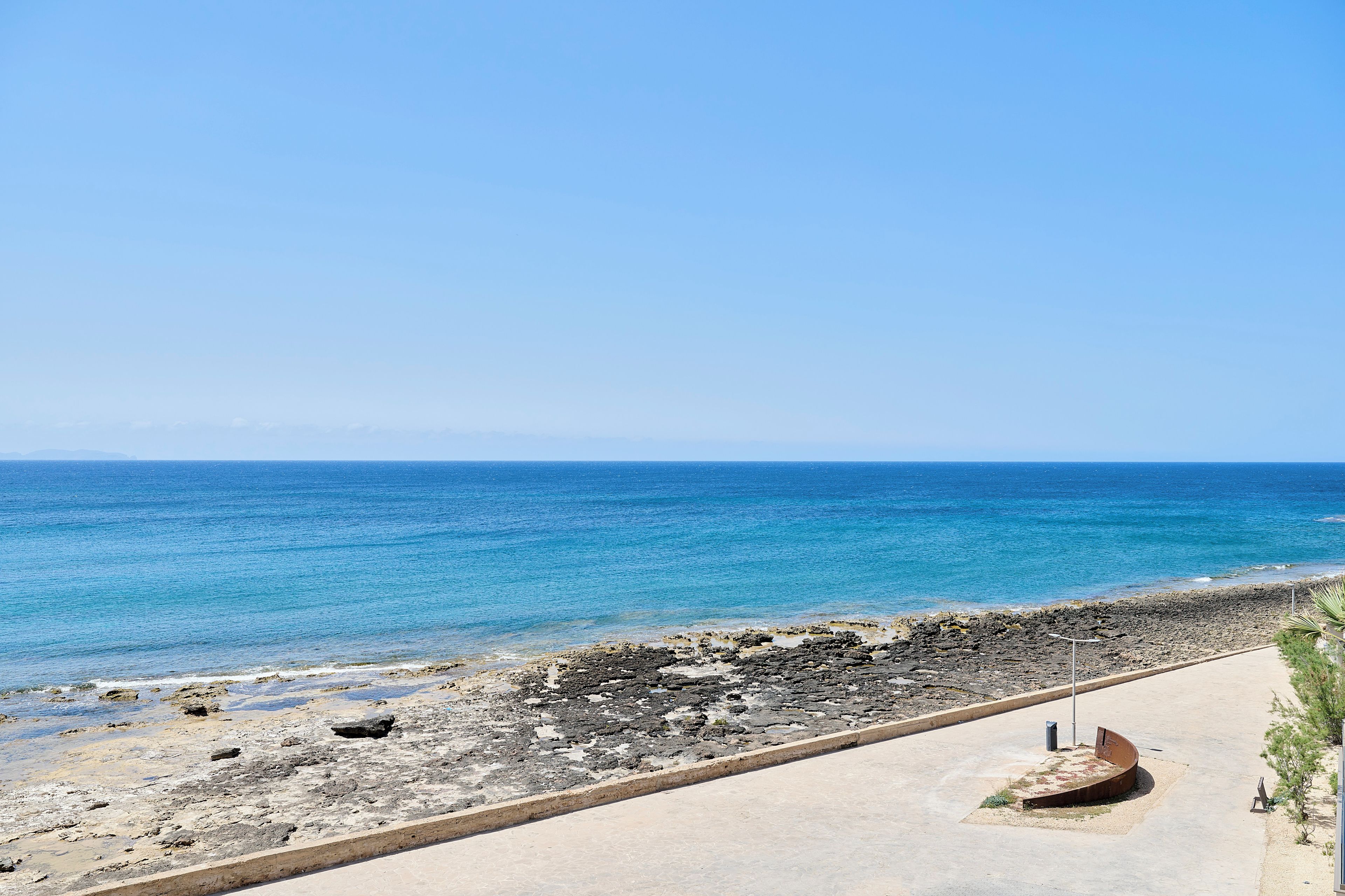 Un paseo marítimo con vistas despejadas al mar, un litoral rocoso y un camino pavimentado.