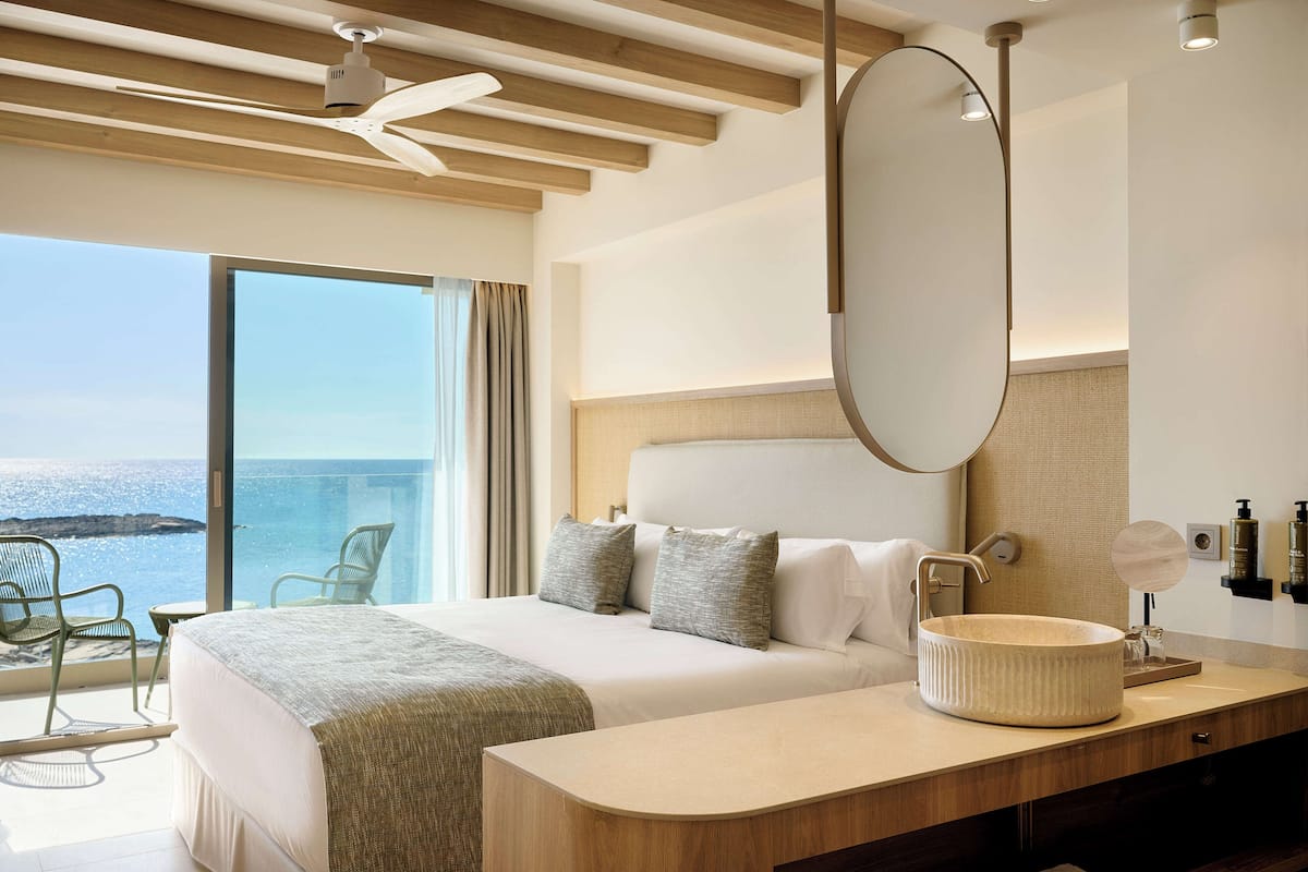 Une chambre d’hôtel avec un grand lit, un miroir rond, un lavabo rond et une vue sur l’océan.