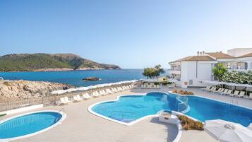 A pool area with multiple swimming pools, lounge chairs, and a view of the sea.