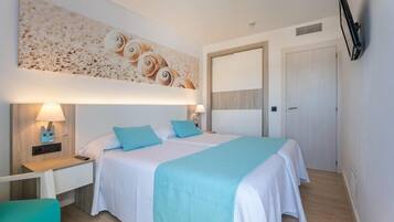 Un dormitorio con cama, mesitas de noche, un televisor montado en la pared y una puerta.