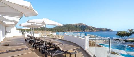 A sun deck with lounge chairs and umbrellas overlooking a pool and the sea.