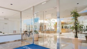 A hotel reception area with glass doors, a reception desk, and a blue mat with the hotel name. - Aparthotel THB Guya Playa (Capdepera)