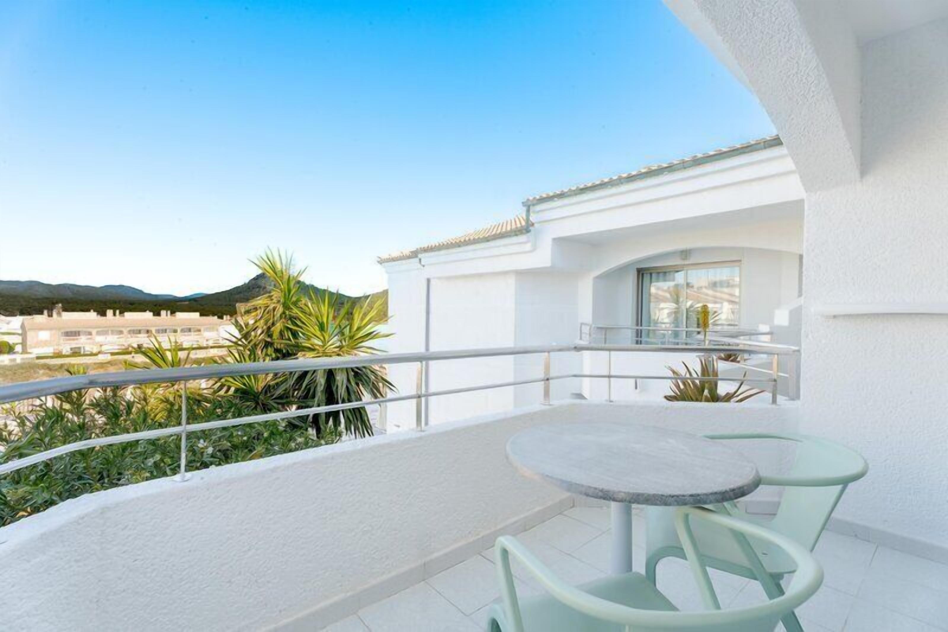 Un balcone con un tavolo rotondo e sedie, una ringhiera bianca e vista sulla città e sulle colline.