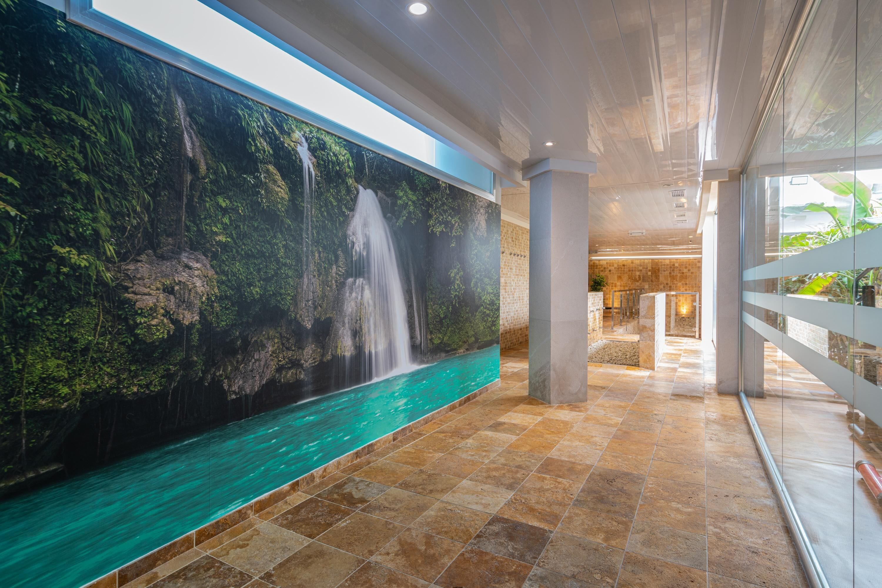 A modern hotel lobby with a large waterfall mural, a checkered floor, and a glass railing.