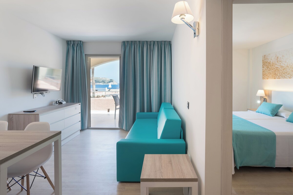 A modern hotel room with a sofa, a bed, a TV, and a desk.