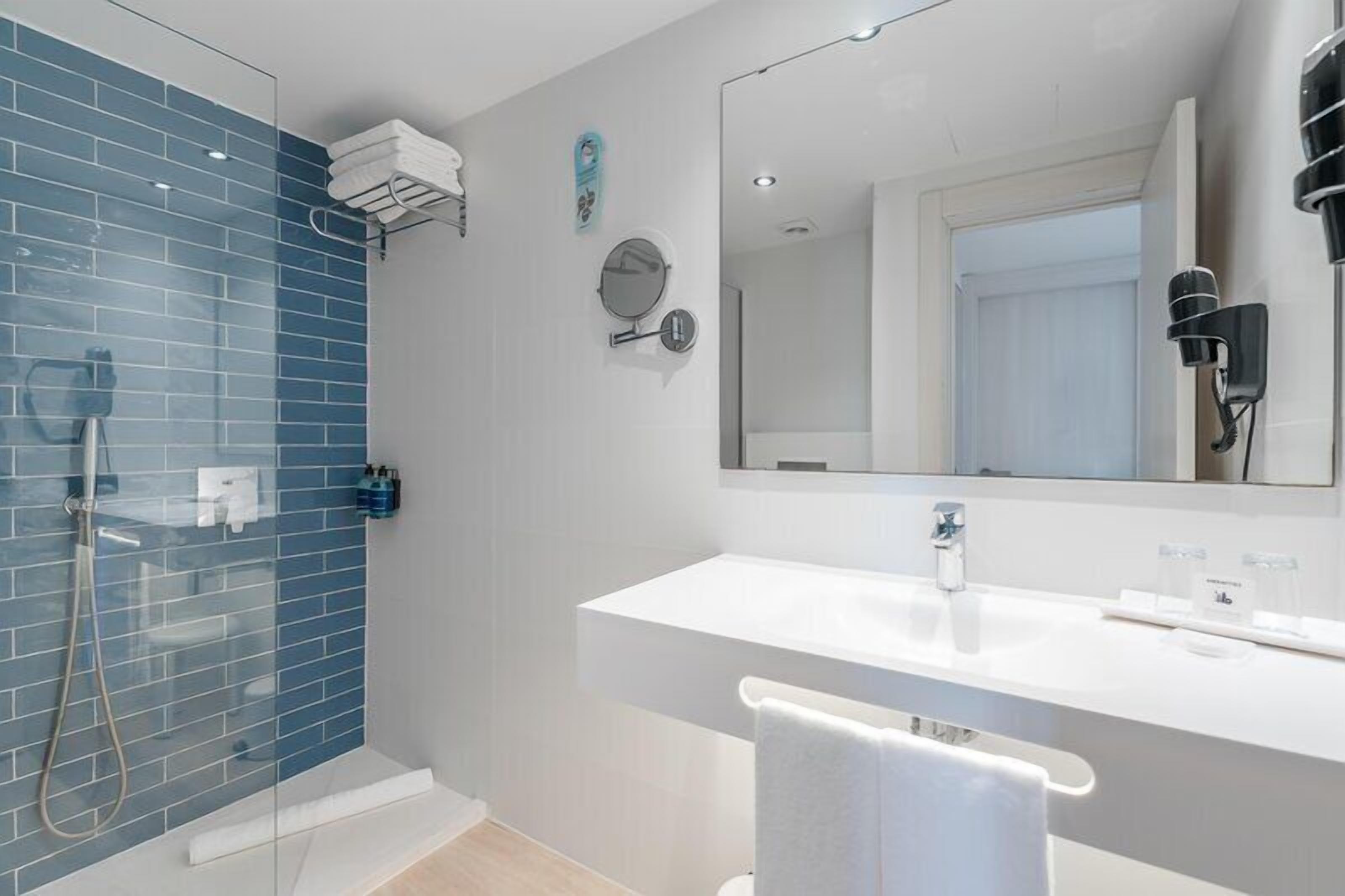 Un baño moderno con cabina de ducha de vidrio, un lavabo blanco y un espejo grande.