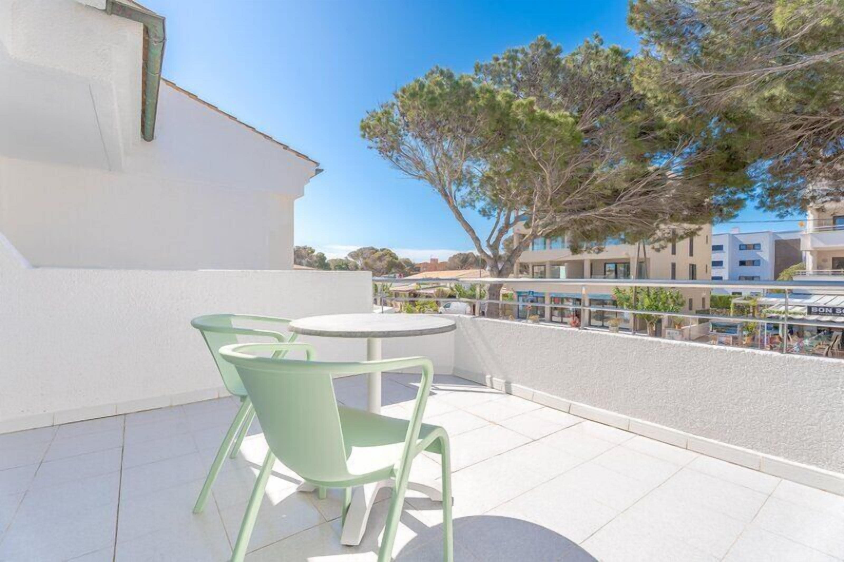 Eine Terrasse mit Tisch und Stühlen, ein weißes Gebäude und Blick auf weitere Häuser und Bäume.