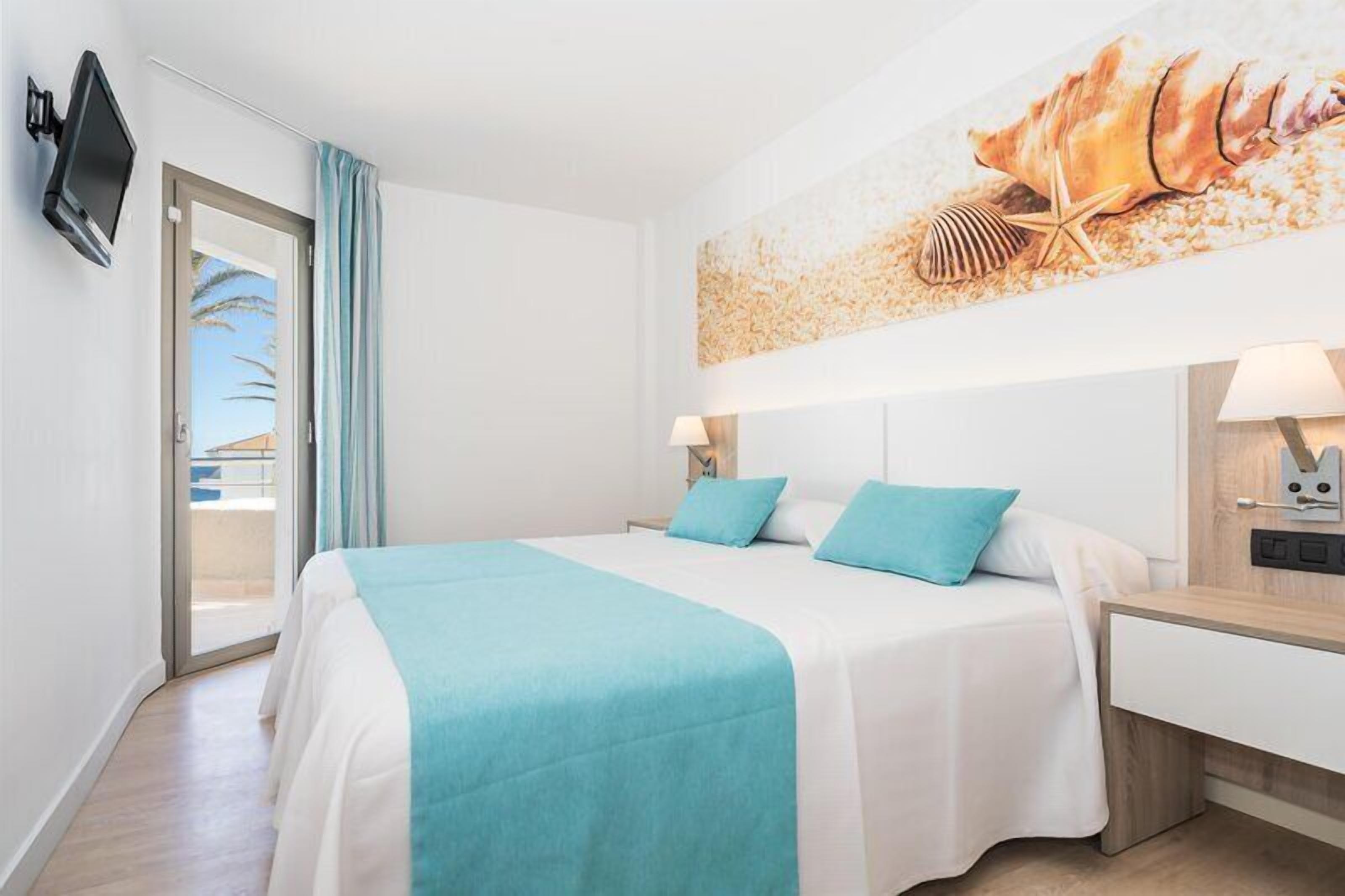 Una habitación de hotel con una cama, televisión, un cuadro y una mesita de noche.