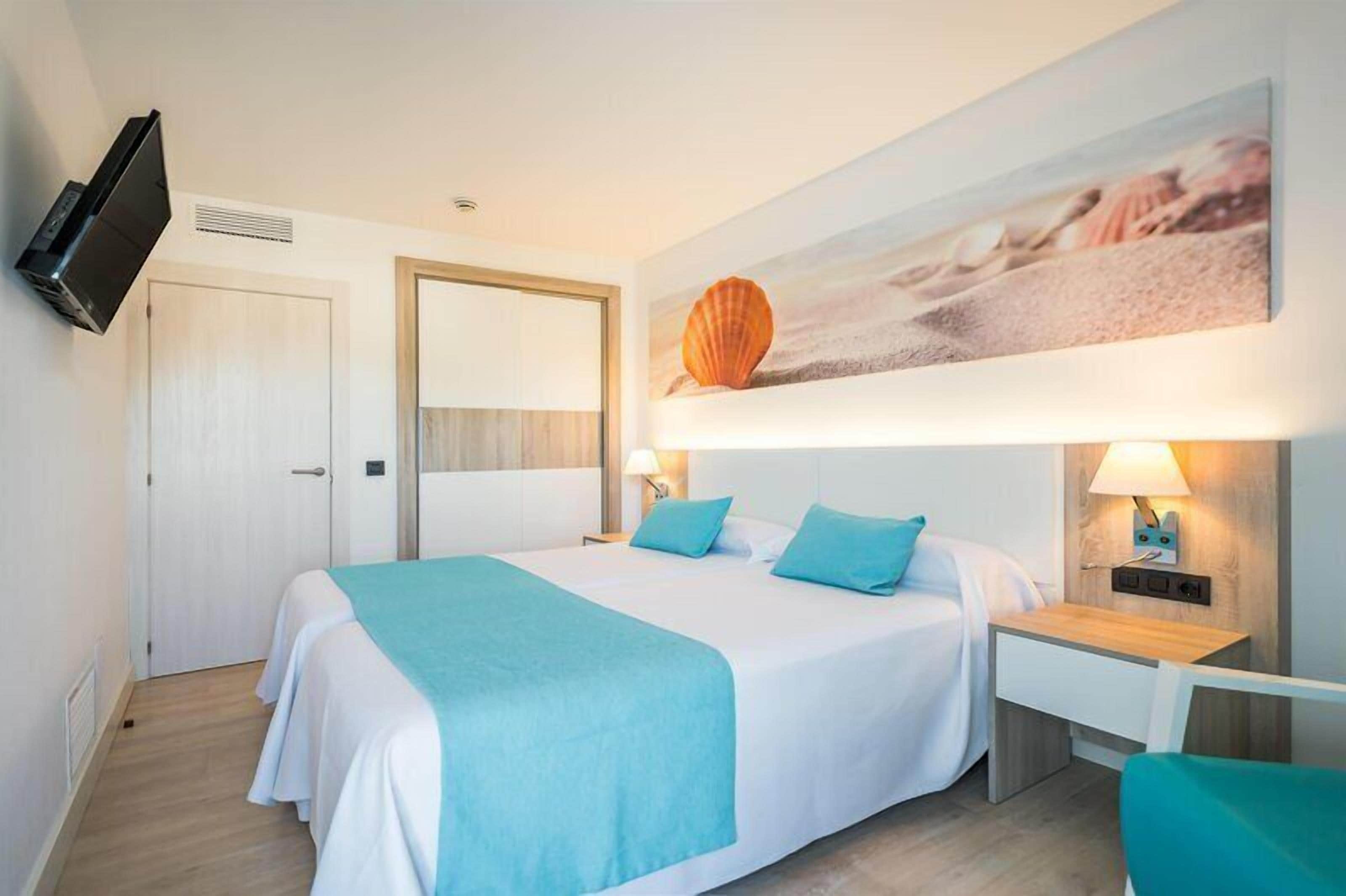 Una habitación de hotel con una cama, mesitas de noche, un televisor, un cuadro y una puerta.